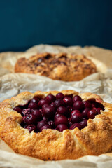 Two galettes with ripe red cherry and walnuts on dark background. Homemade sweet open pie.