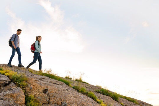 Couple of Young Happy Travelers Hiking with Backpacks on the Rocky Trail at the Evening. Family Travel and Adventure