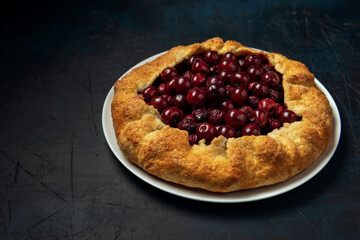 Galette with ripe red cherry filling on dark blue background. Homemade sweet open pie. Space for text.