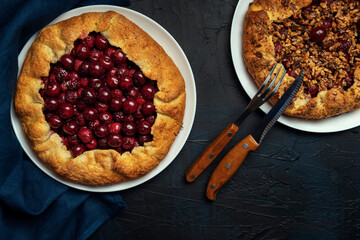 Two galettes with ripe red cherry and walnut filling on dark blue background. Homemade sweet open pie with napkin and cutlery. Top view.