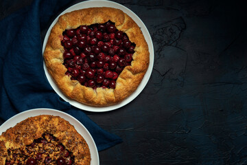 Two galettes with ripe red cherry and walnut filling on dark blue background. Homemade sweet open pie. Top view. Space for text.