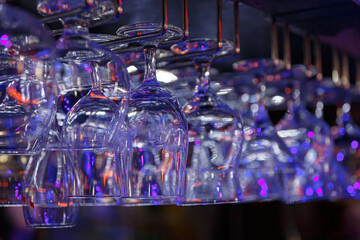 Empty wine glasses hanging over a bar rack in a nightclub.