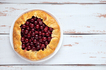 Galette with ripe red cherry filling on white background. Homemade sweet open pie on Provence style background. Top view. Space for text.