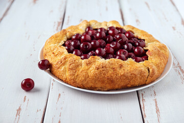 Galette with ripe red cherry filling on white background. Homemade sweet open pie on Provence style background.