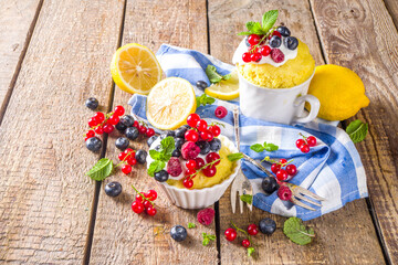 Lemon Mug Cake. Summer sweet dessert in  Microwave. Lemon Mug Pies with fresh berries and whipped cream, on wooden background