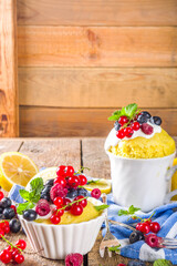 Lemon Mug Cake. Summer sweet dessert in  Microwave. Lemon Mug Pies with fresh berries and whipped cream, on wooden background
