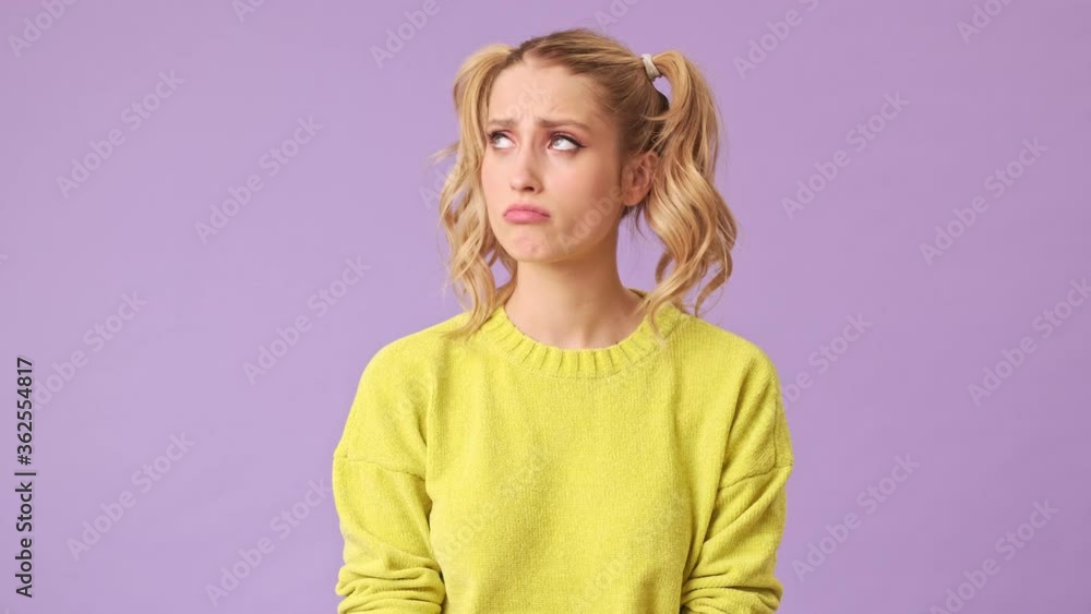 Poster a beautiful sad blonde in a yellow sweater looks sadly at the floor in an isolated studio on a purpl