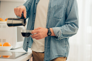 Man in jeans shirt pouring hot coffee from the coffee pot
