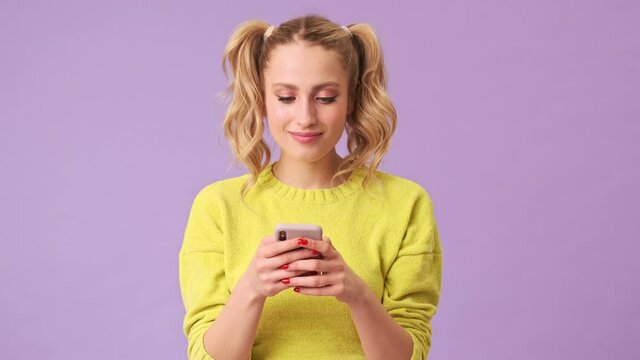 A magical blonde girl smilingly writes a message on the phone in an isolated studio on a purple background