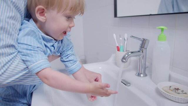 Close up mother wash liquid soap hands little baby ln bathroom in pajamas. Clean hands. Mom washes hands preschool child