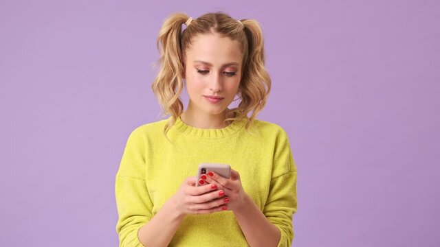 An incredible blonde girl writes a message to her friend on the phone, winks and sends a kiss to the camera in an isolated studio on a purple background