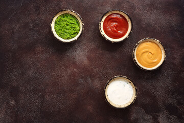 Collection of various sauces in the bowl: tomato, pesto, creamy with greens and mustard on a dark rustic background. Top view, copy space.