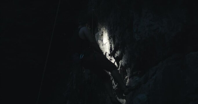 Climber with mustache climb up ascend reach top with hand hold grip wear headlamp light descend rappel in stone rock wall at night