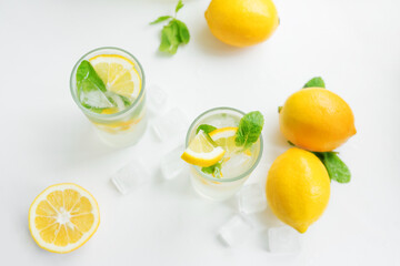 Two Foggy glasses and a decanter with homemade lemonade and lemons on a white table. Cooling drink in the hot summer. Lemons, mint and ice. Top view.