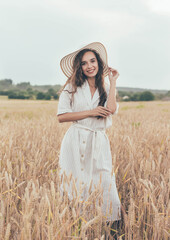 
Portrait of a girl on a wheat field in a hat and dress, a girl on a wheat field holds a hat in her hands and laughs