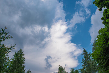 Dramatic group of clouds in a blue sky before rain surrounded by green foliage as a background.