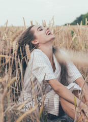 
portrait of a girl of model appearance in wheat, a girl sits in a wheat field and smiles - obrazy, fototapety, plakaty