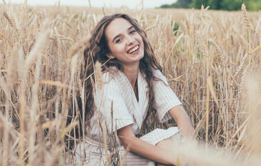 
portrait of a girl of model appearance in wheat, a girl sits in a wheat field and smiles
