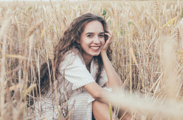 
portrait of a girl of model appearance in wheat, a girl sits in a wheat field and smiles