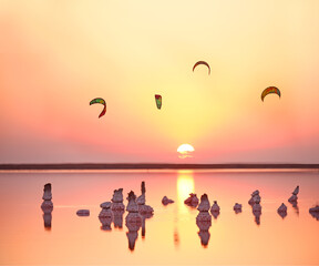 Sunset on the pink lake. Columns in crystals of salt in water and kitesurfers against the setting sun.