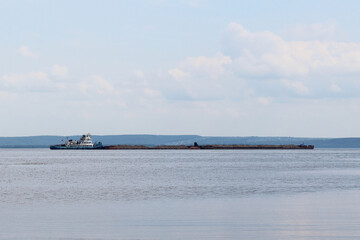 Barge with cargo floating on the river. Vehicles for transporting sand, gravel or rubble. Background. Landscape.