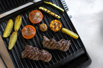Electric grill with roast beef, spicy potatoes, mushrooms and vegetables