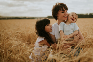 family portrait of a mother and two children sitting in a wheat field under a sunset