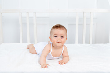 smiling baby girl 6 months old lying on the bed in the nursery on her stomach and looking at the camera, morning baby, baby products concept
