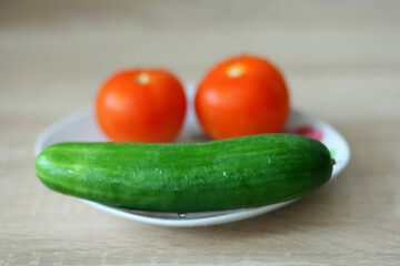 Two red tomatoes and a green cucumber are on a nice plate