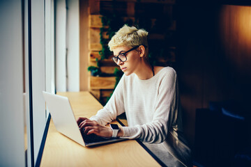 Concentrated female copywriter typing on laptop computer text for publication on web page,...
