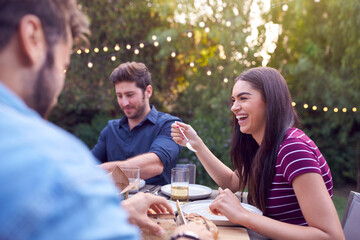 Multi-Cultural Friends At Home Sitting At Table Enjoying Food At Summer Garden Party