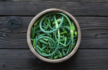 Garlic arrows in a wooden bowl on a dark wooden table. Chopped garlic shoots for cooking. Gourmet seasoning