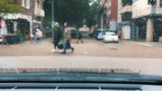 Pedestrians cross the road.View from inside the car to outside.  Rain drops on car windshield.  Blur background and texture traffic on the road In rainy season.