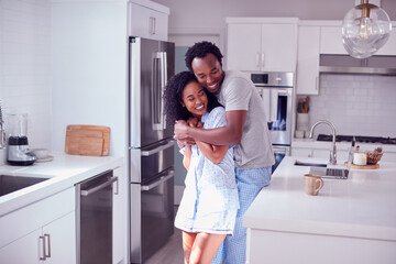 Loving Couple Wearing Pyjamas Hugging In Kitchen At Home Together