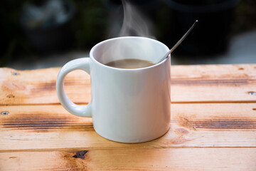 Coffee and steam in a white mug on a wooden table
