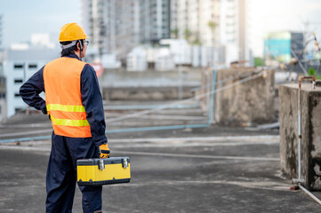 Asian maintenance worker man wearing protective suit and safety helmet carrying work tool box at construction site. Equipment for civil engineering project
