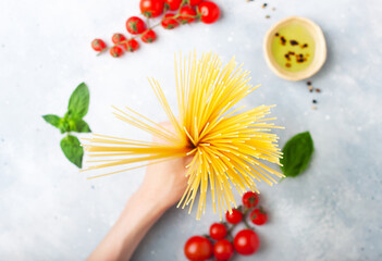 Italian food - female hand holding raw spaghetti: pasta ingredients concept on grey stone background, flat lay
