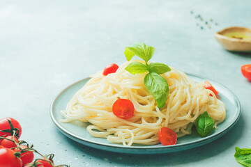 Italian food - spaghetti pasta decorated with cherry tomatoes, olive oil, basil and spices on grey blue background, copy space, closeup