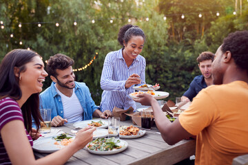 Multi-Cultural Friends At Home Sitting At Table Enjoying Food At Summer Garden Party