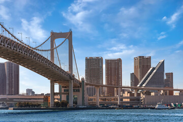 Naklejka premium Double-layered expressway of the suspension Rainbow Bridge in the Tokyo Bay with a tugboat sailing in Tokyo port and the skyscrapers of the Shibaura-futō district in back