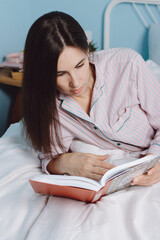 Cropped view of young calm brunette millennial smart cheerful mixed race woman student relaxing reading book lying on bed with white sheets at home or hotel. Beautiful girl enjoys her freetime indoor