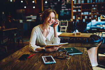 Portrait of cheerful female designer analyzing information from project plan having creative idea, charming businesswoman enjoying working process on successful startup sitting in coffee shop