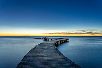 Sea shore scenic walkway bridge under sunset glow with rosy clouds.