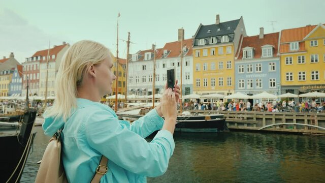 Woman take pictures of Nyhavn canal, against the background of famous colorful houses.