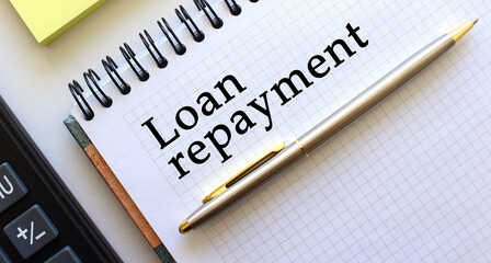 Notepad with text LOAN REPAYMENT, next to it lies a calculator and yellow note papers. Business concept.