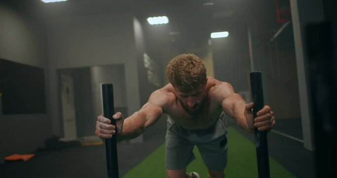 a tenacious single-minded male athlete pushes a heavy sled in the gym. exercise with a heavy weight for endurance