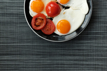 plate of fried eggs with tomato on dark background, top view