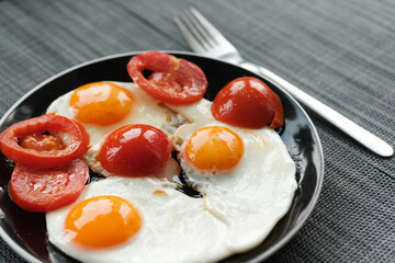 plate of fried eggs with tomato on dark background, top view