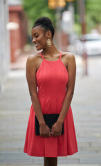 Beautiful business woman in coral colored dress stands in shade on city street holding tablet computer