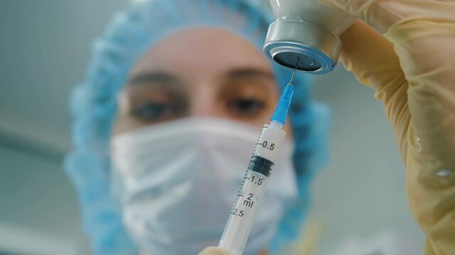 Doctor fills in syringe liquid vaccine from glass vial, close up